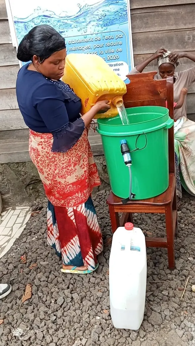 A mother in Goma pours water into a shared filter