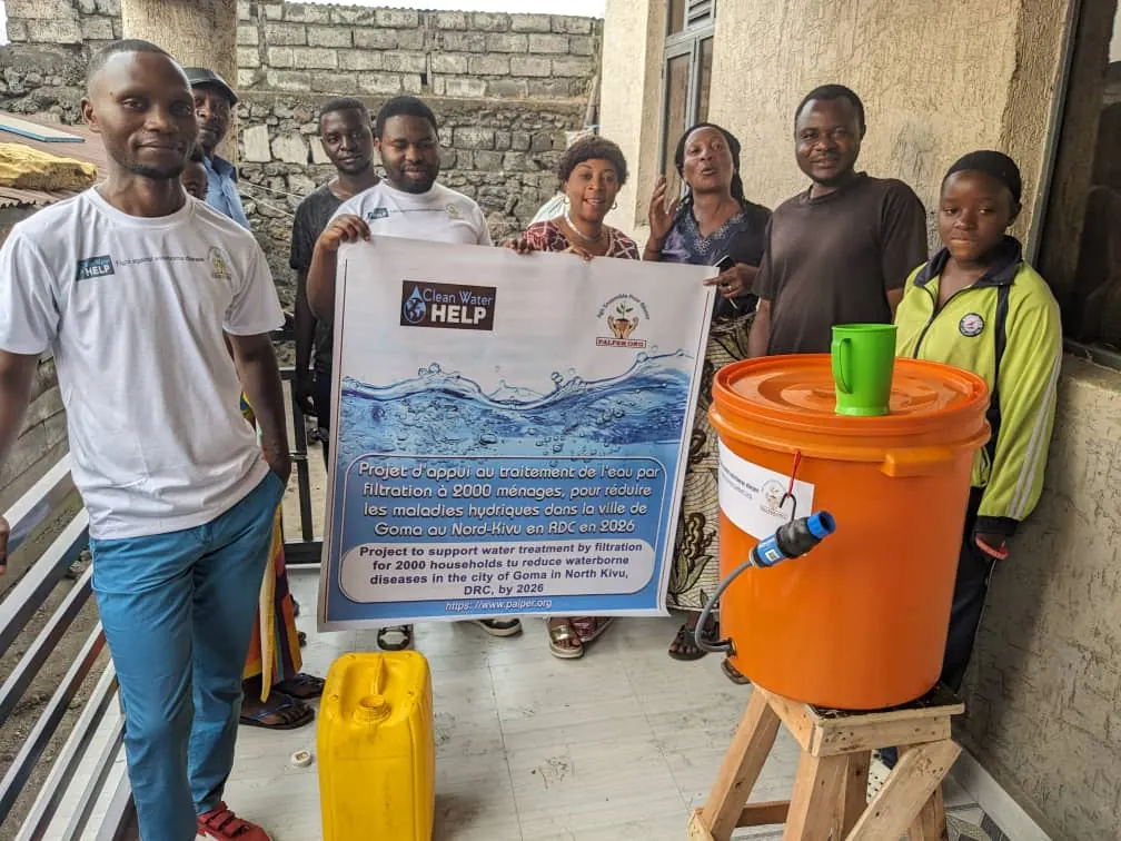 A household group with PALPER staff around their new orange filter, holding the project banner