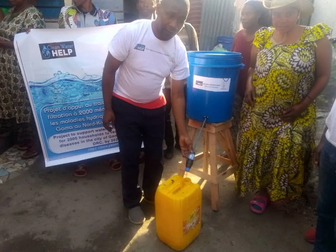 Filtered water runs from the tap of a blue bucket filter into a yellow jerrycan