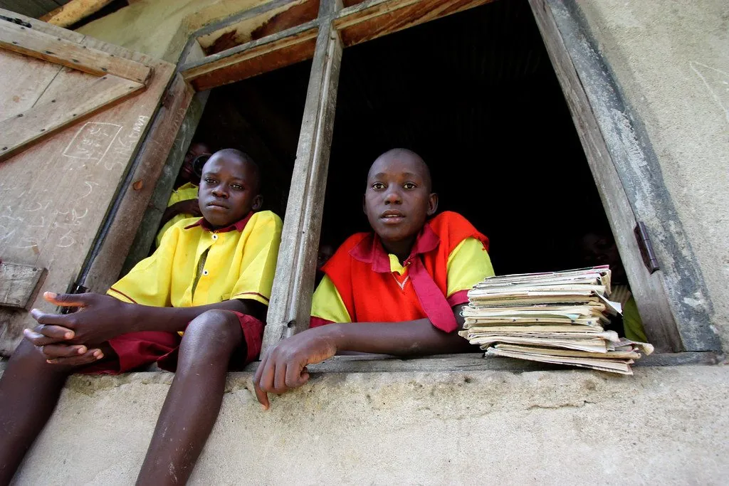 Two students with a stack of exercise books at a school window in DR Congo